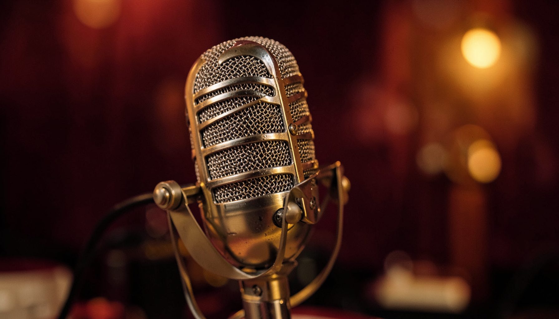 Primer plano de un micrófono de estudio vintage sobre un fondo cálido en tonos granate y dorado, con un ambiente íntimo