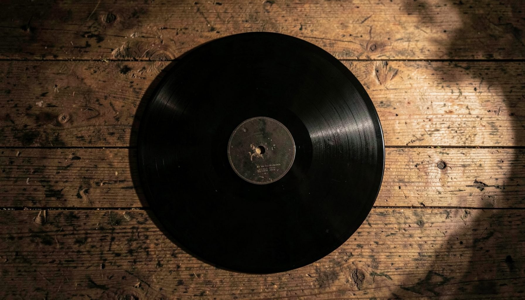 Un vinilo negro sobre una superficie de madera envejecida, iluminado por una luz cálida y tenue.