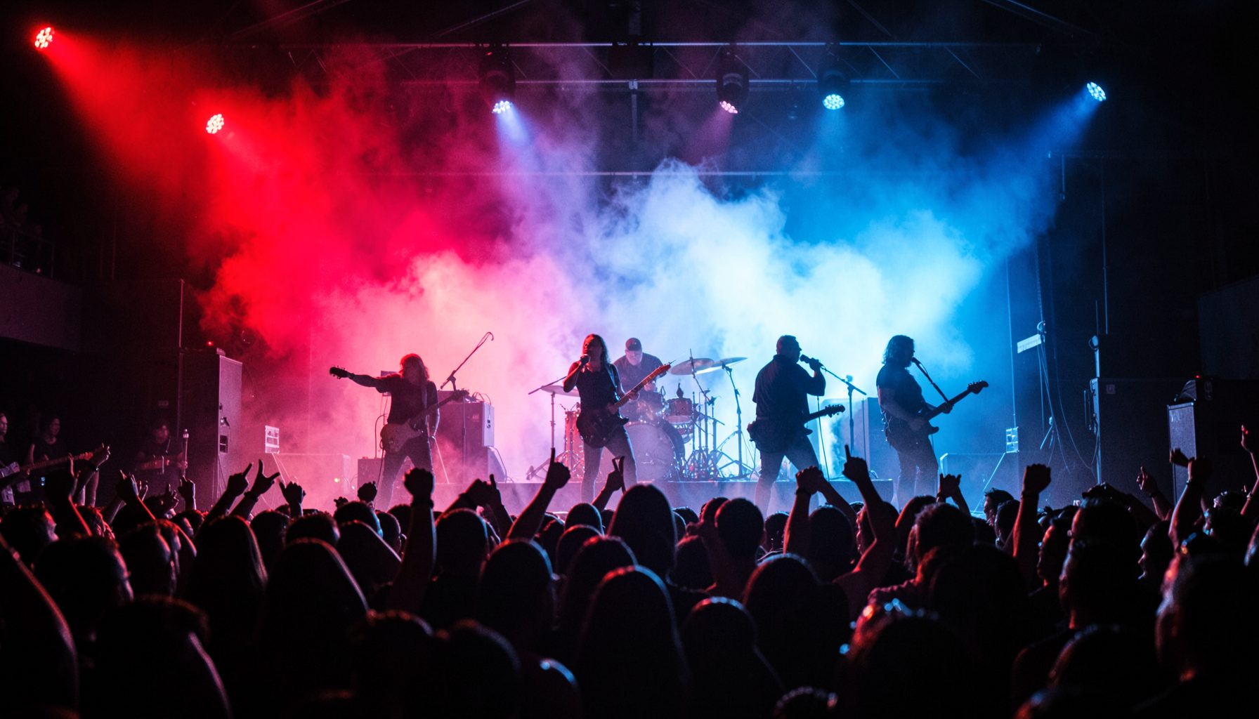 Escenario de un concierto de rock con luces rojas y azules, humo denso y siluetas de músicos tocando ante un público entregado