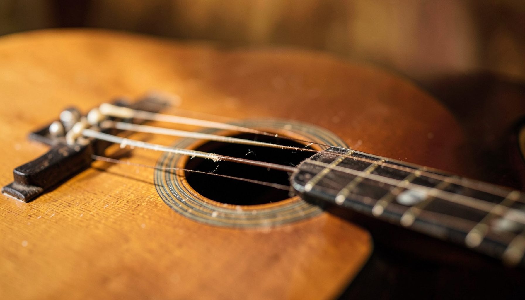 Primer plano de una guitarra acústica con cuerdas desgastadas sobre un fondo cálido de tonos marrones y dorados, luz suave
