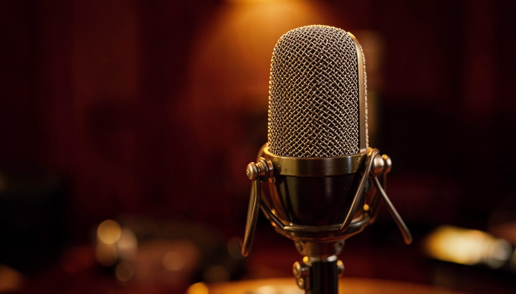 Primer plano de un micrófono de estudio vintage sobre un fondo cálido en tonos granate y dorado, ambiente íntimo