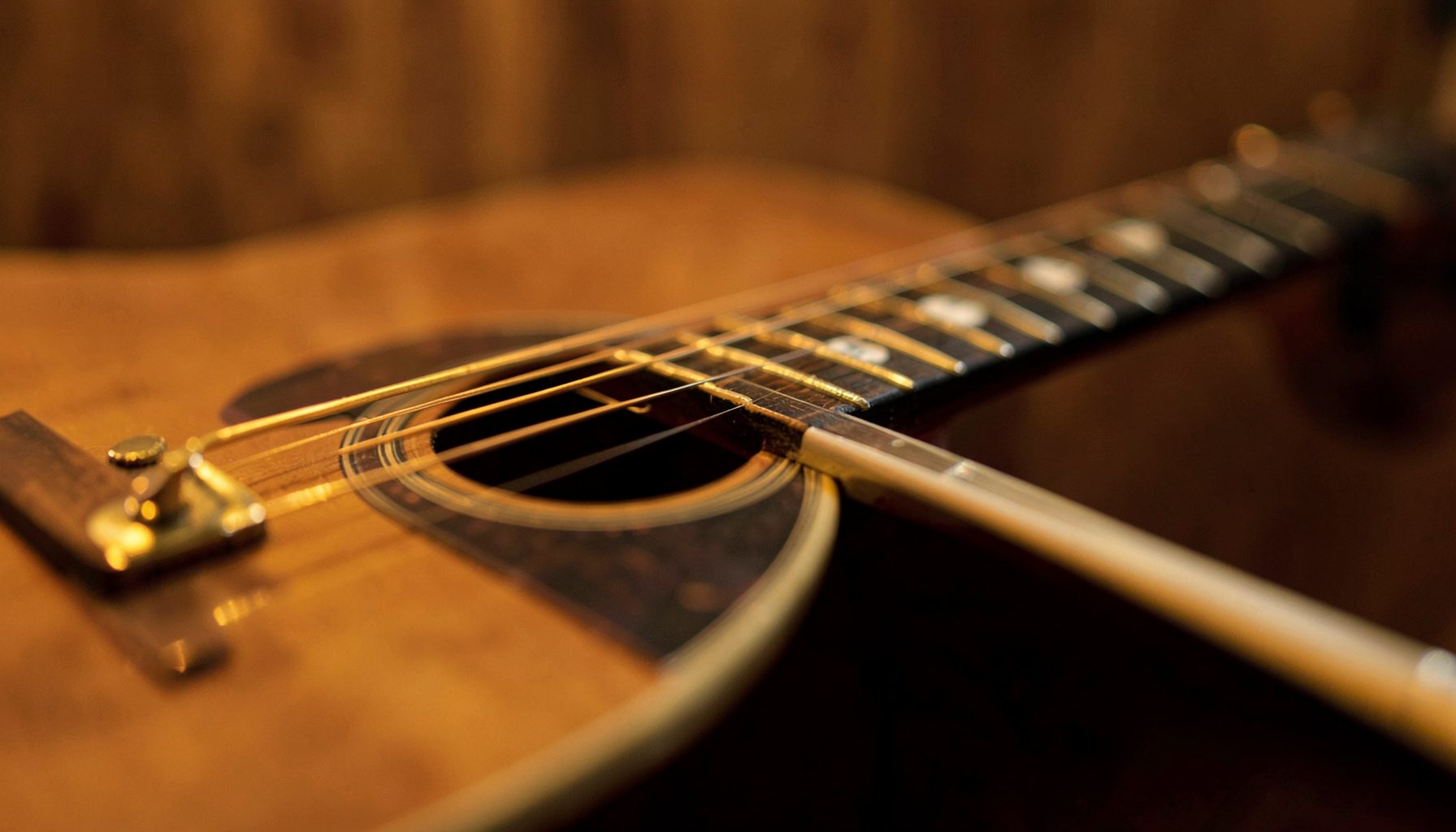 Primer plano de una guitarra acústica con cuerdas doradas sobre un fondo cálido de tonos marrones y ámbar, con una luz suave y envolvente